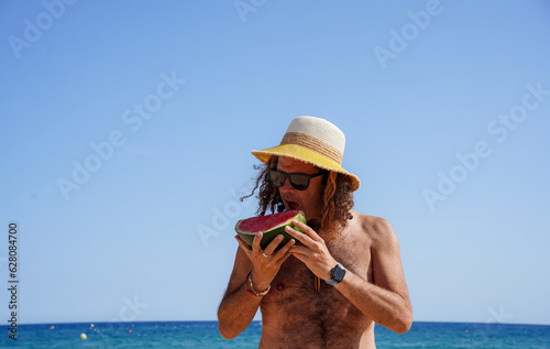 Portrait of an old man with a hat on the beach eating watermelon. Toxic and price increase in watermelon