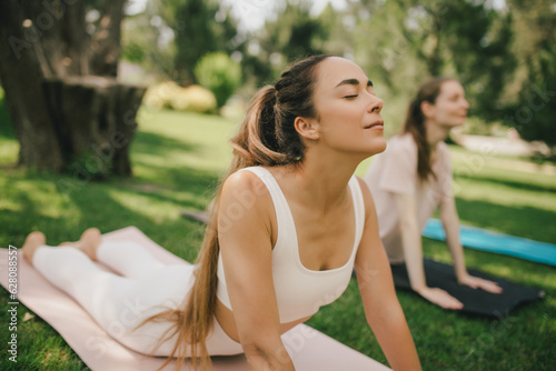 Group of millennial women having group yoga class in a park. Healthy lifestyle.