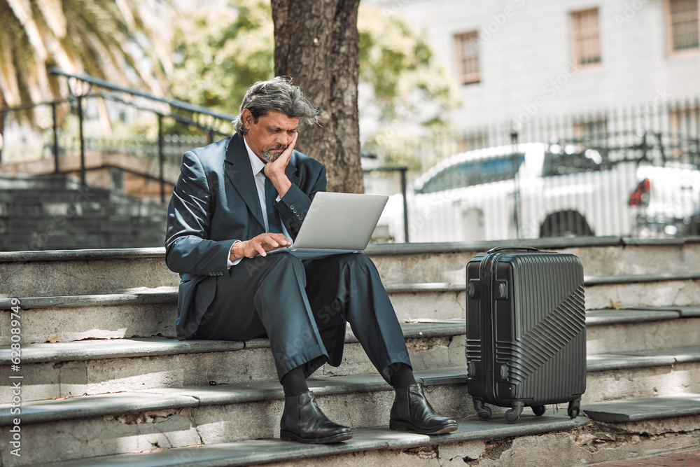 Travel, email and businessman with laptop in the city for communication and booking a flight online. Serious, working and mature corporate manager with a computer and luggage for a ticket on the web Travel, email and businessman with laptop in the city for communication and booking a flight online. Serious, working and mature corporate manager with a computer and luggage for a ticket on the web