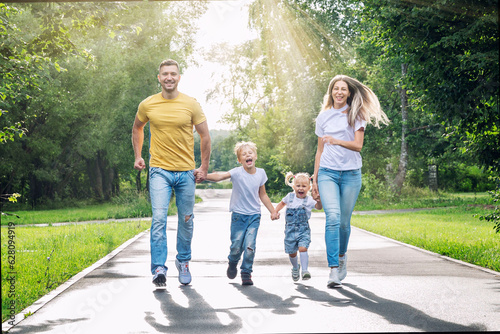 Happy family with two children joyfully run in the park on a sunny summer day. Parents, son and daughter in jeans and T-shirts. Love, tenderness and relationships in the family. © Анна Демидова