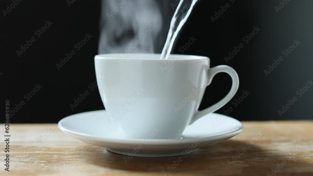 A hot cup of coffee with steam stands on a wooden table on a black background A hot cup of coffee with steam stands on a wooden table on a black background
