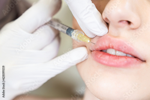 A young woman gets injection of botox in her lips. Woman in beauty salon. Plastic surgery clinic.