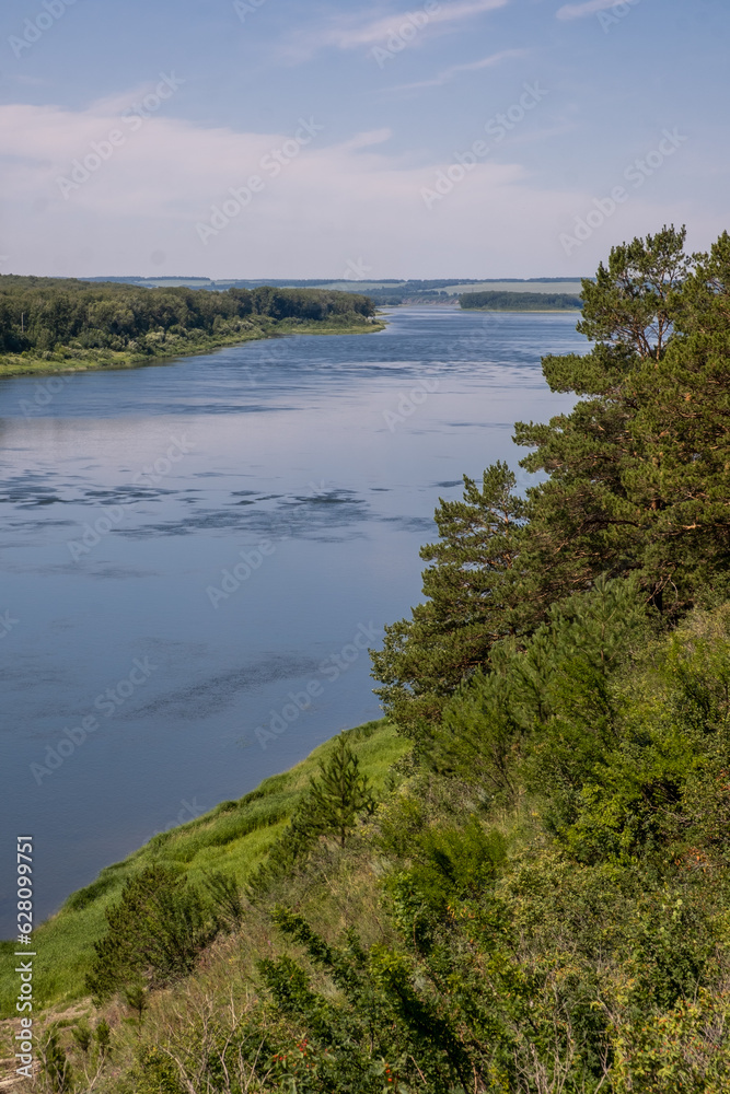 Beautiful, wide autumn river among forests and rocky shore. A calm and quiet place with autumn colors. Reflection of clouds in the water in good weather