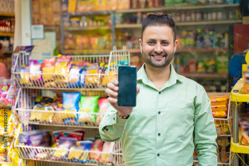 Young indian man showing smartphone screen at grocery shop.