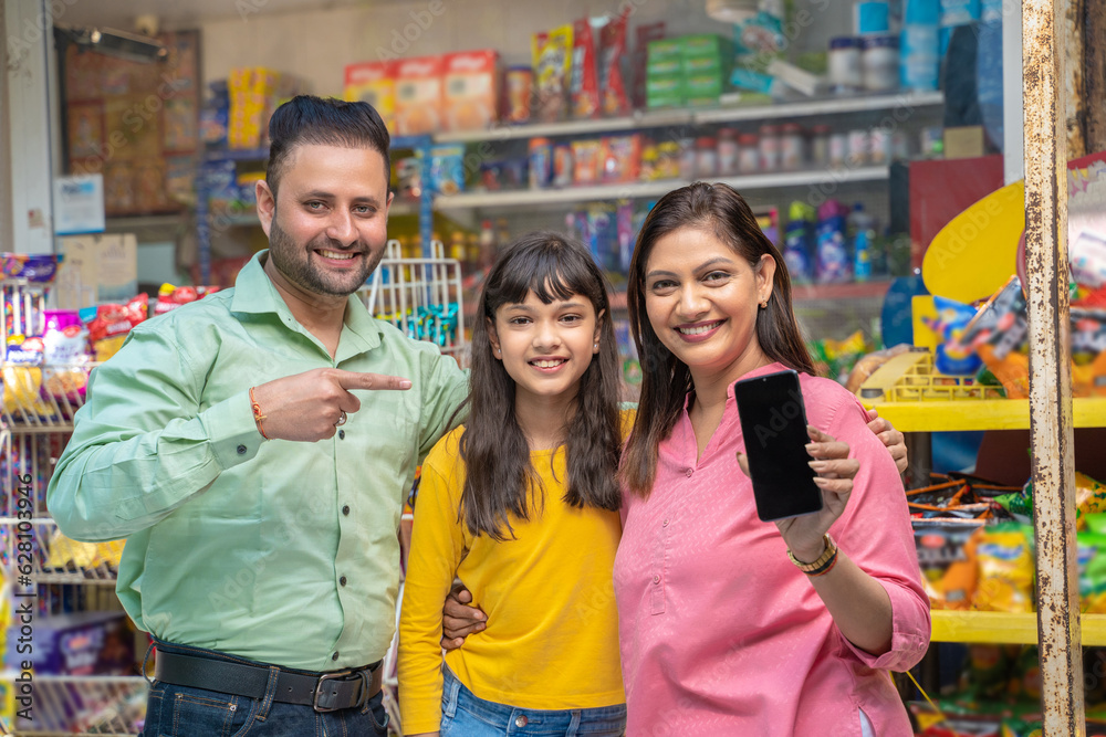 Obraz premium Happy indian family showing smartphone Screen at grocery shop.