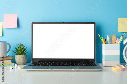 Desk of student during online education concept. Side view photo of white desk with laptop and stationery on isolated blue background with copy-space for text or advertising