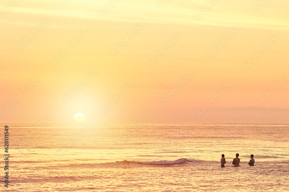 Silhouettes of a young group of people swimming in the ocean at sunset