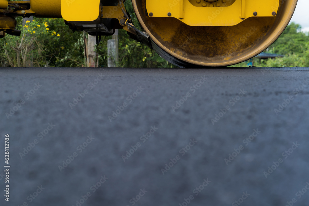 Yellow heavy vibrating roller on asphalt pavement Road construction, repairing rural road, sunny summer day. heavy equipment