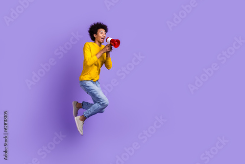 Full length size view photo of funny crazy man jumping with megaphone loudspeaker proclaim announce isolated on violet color background photo