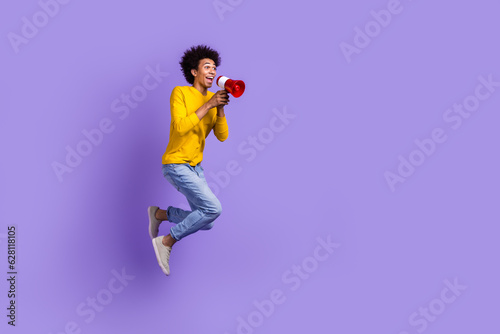 Full length size view photo of funny crazy man jumping with megaphone loudspeaker proclaim announce isolated on violet color background photo