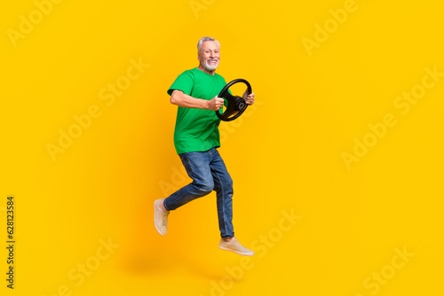 Full body profile portrait of crazy cheerful handsome man jumping hands hold wheel empty space isolated on yellow color background © deagreez