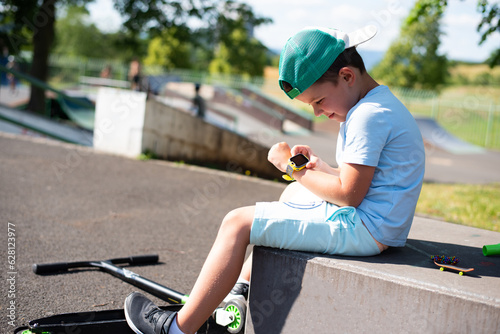 A little 7 year old boy in bright summer clothes looks at his yellow smart watch on his hand