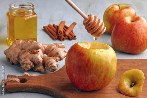 Red apple and spoon with dripping honey on background of ingredients on blue wooden table. Cooking baked apples with honey, cinnamon and ginger photo