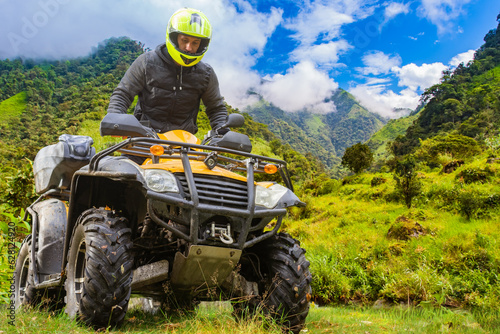 Man on ATV. Guy drives off-road. Four-wheel motorcycle driver. Quad biker in picturesque place. ATV for extreme recreation. Man in yellow helmet sits on quad bike. ATV with driver in sunny weather