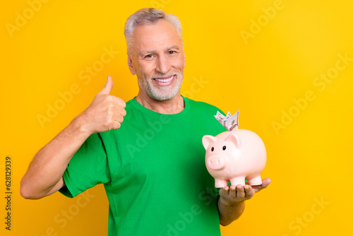 Foto Photo of satisfied aged man toothy smile hold money pig bank demonstrate thumb u