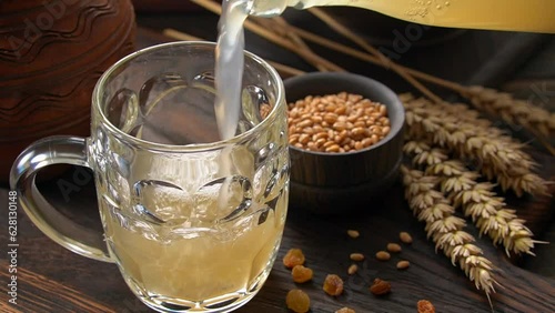 Pouring white wheat kvass into mug. Fermented russian traditional beverage. photo