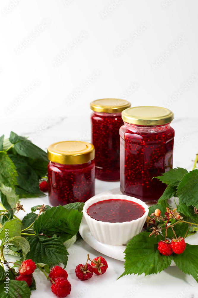 Homemade summer preservation, raspberries jam in jars, jars with jam and raspberry sprigs
