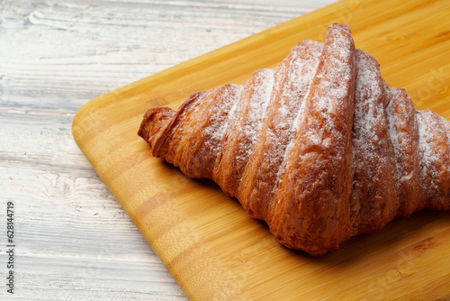 Freshly baked croissant with powdered sugar on wooden board