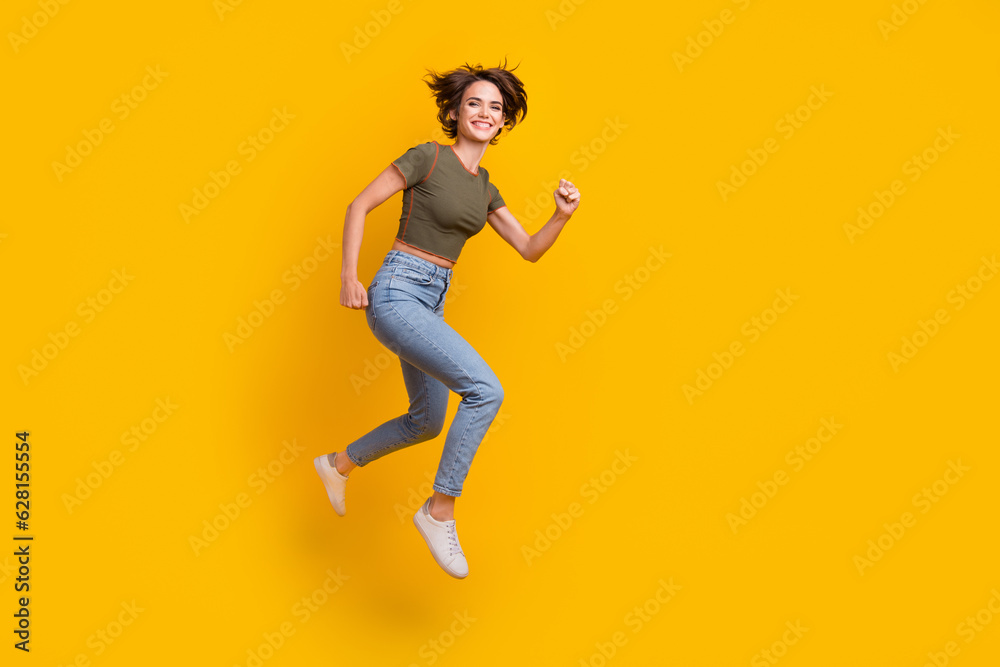 Full length photo of adorable excited girl dressed khaki top jumping high running empty space isolated yellow color background