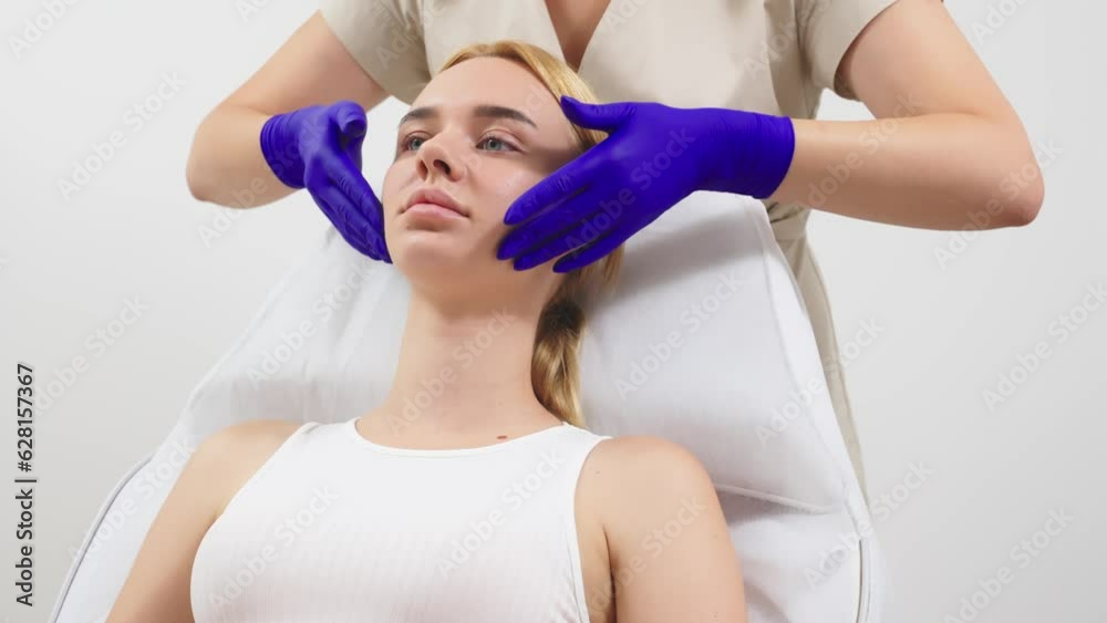 Beautiful young woman receiving the cosmetic procedures in the beauty salon, cosmetologist doing smoothing hand movements on her face. Beautiful young woman receiving the cosmetic procedures in the beauty salon, cosmetologist doing smoothing hand movements on her face.
