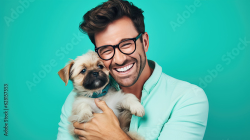 Young man holds a dog puppy in his arms on blue background.
