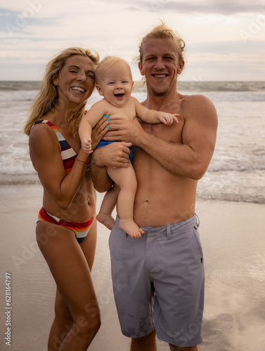 Happy family spending time on the beach. Father and mother holding infant baby boy. Mum, dad and son smiling. Positive emotions. Summer vacation. Family beach concept. Seminyak beach, Bali