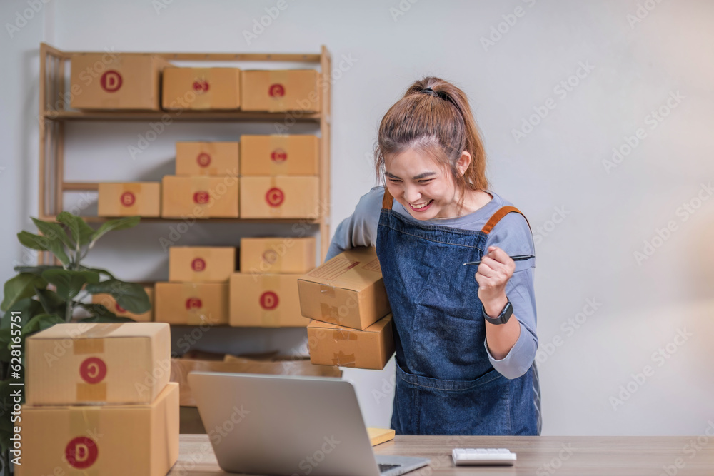 Startup SME small business entrepreneur of freelance Asian woman using a laptop with box Cheerful success Asian woman her hand lifts up online marketing packaging box