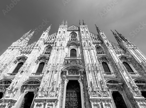 Frontal facade of Milan cathedral or “Metropolitan Cathedral-Basilica of the Nativity of Saint Mary“ in northern Italy. Wide angle view of world famous church from frog perspective. Black and white. photo