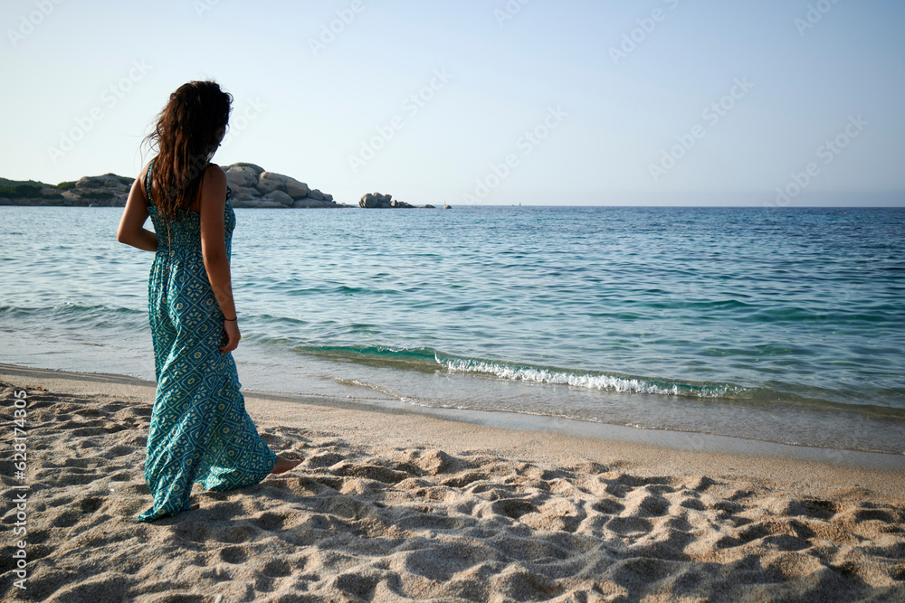 A beautiful young woman walking on the beach wearing a blue dress A beautiful young woman walking on the beach wearing a blue dress