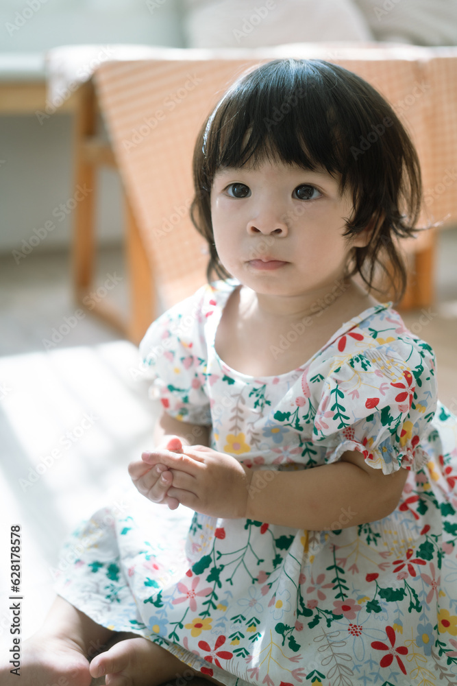 A cute caucasian baby girl with big eyes and black hair in white colorful dress, looking to the camera. People portairt photo. A cute caucasian baby girl with big eyes and black hair in white colorful dress, looking to the camera. People portairt photo.