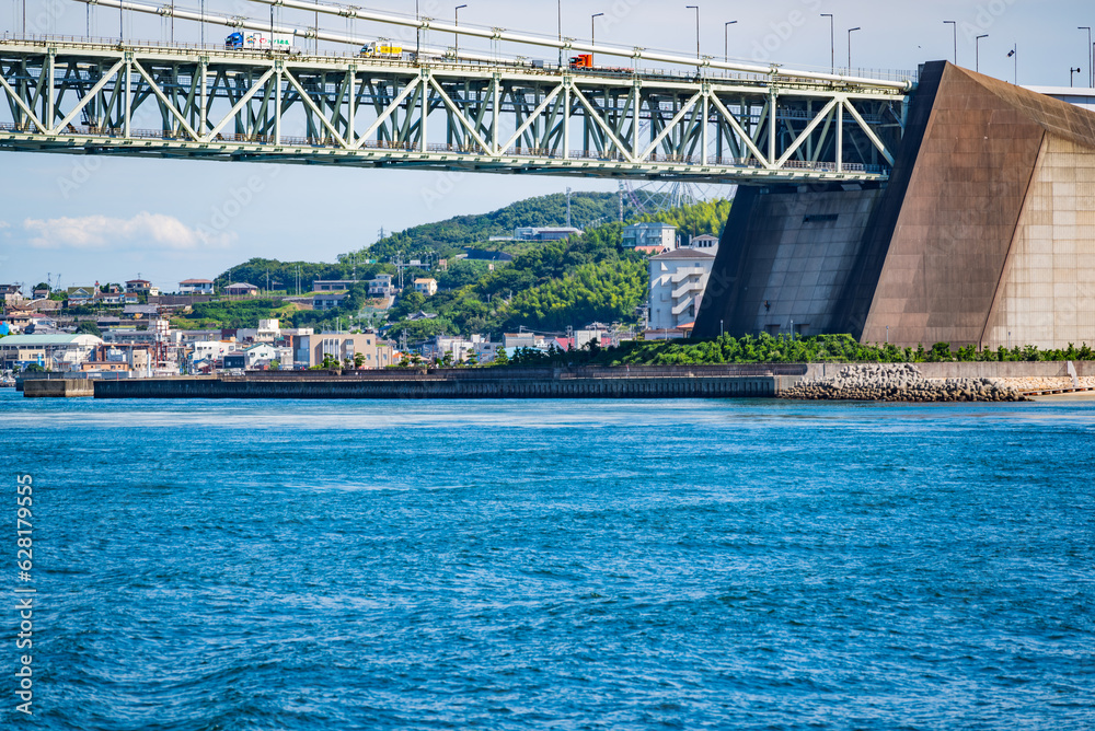 Fototapeta premium フェリーの上から見た明石海峡大橋の橋脚部分(淡路島側)と漁港町である岩屋の風景