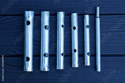a set of a row of gray metal tubular wrenches lie on a black wooden table photo