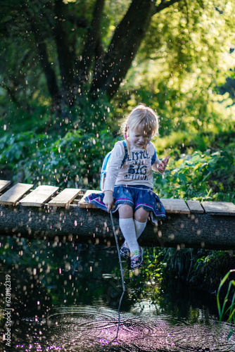 Fototapeta Naklejka Na Ścianę i Meble -  funny little girl catches fish in the stream sitting on the bridge, beautiful backlight