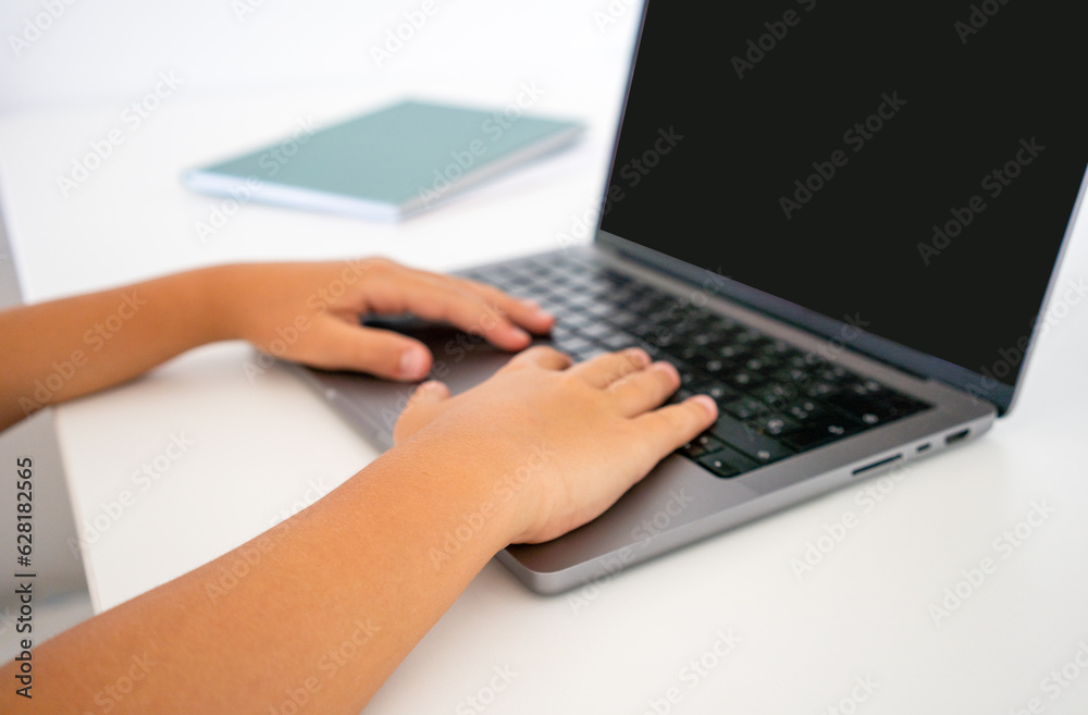 Close-up cropped shot of unrecognizable child boy typing on laptop keyboard and surfing internet sitting at desk. Pupil boy studying remotely at home. Schoolboy pushing fingers on keys of laptop. Close-up cropped shot of unrecognizable child boy typing on laptop keyboard and surfing internet sitting at desk. Pupil boy studying remotely at home. Schoolboy pushing fingers on keys of laptop.