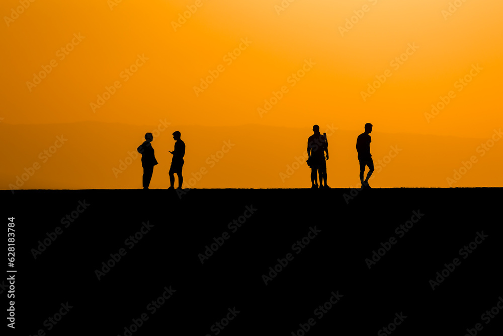 Silhouette of tourists on a sea wall watching a spectacular orange sunset