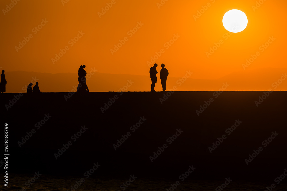 Silhouette of tourists watching the sun set behind a distant mountain in summer