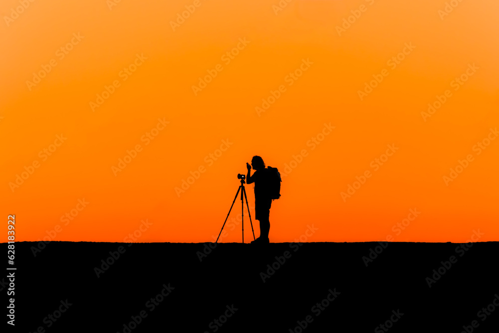 Silhouette of a lone photographer with tripod taking an image during a beautiful orange sunset