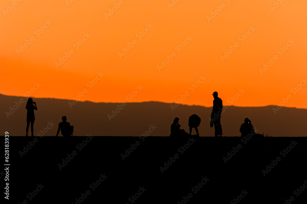 Silhouette of tourists on a sea wall watching a spectacular orange sunset