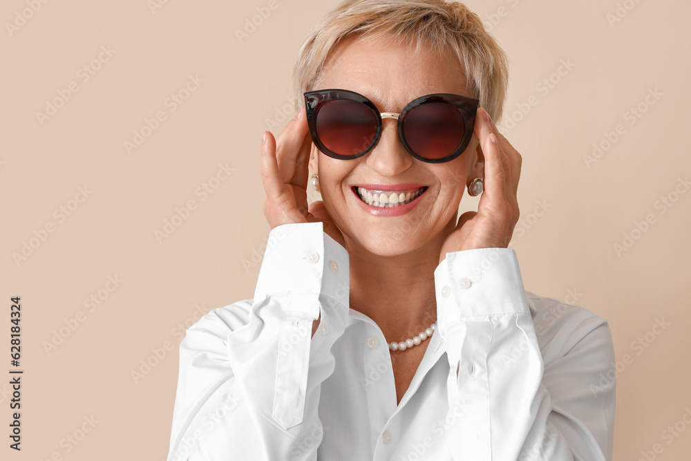 Beautiful mature woman in sunglasses on beige background, closeup Beautiful mature woman in sunglasses on beige background, closeup