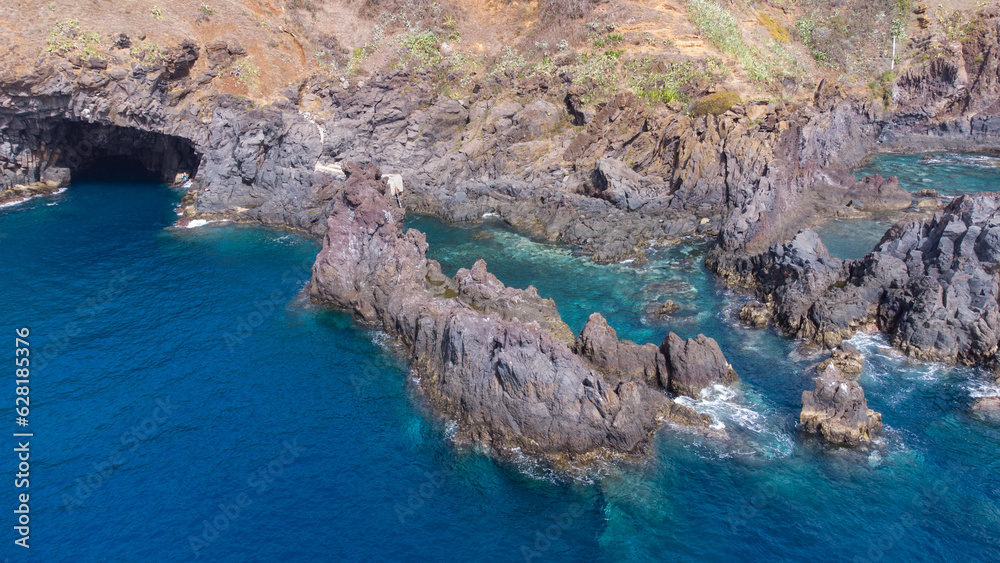Obraz premium Aerial view of rocky cliffs on the coast of Madeira at the Atlantic ocean with clear blue water