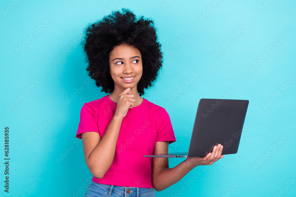 Photo of charming child with afro chevelure wear pink t-shirt hold laptop hand on chin look empty space isolated on blue color background Photo of charming child with afro chevelure wear pink t-shirt hold laptop hand on chin look empty space isolated on blue color background