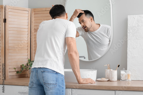 Photography Worried young man with hair loss problem looking in mirror at home