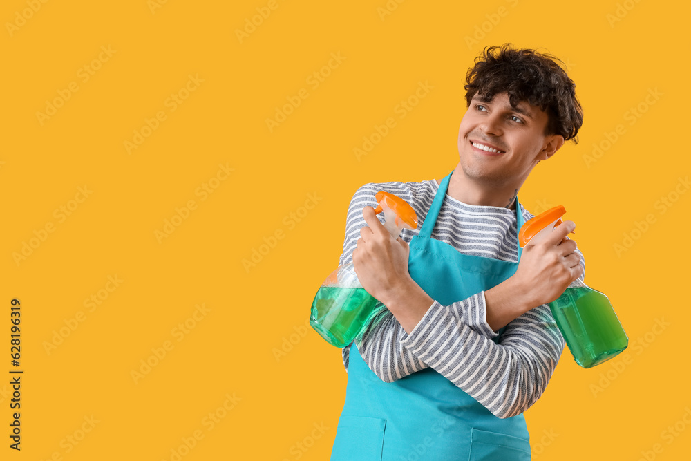 Young man with spray bottles of detergent on yellow background Young man with spray bottles of detergent on yellow background