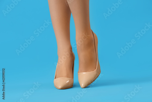 Legs of beautiful young woman in beige tights and high heels on light blue background