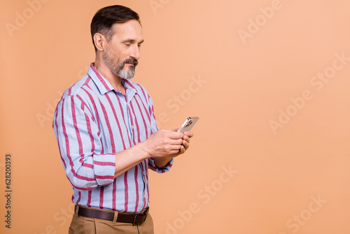 Portrait of handsome positive person with white gray beard striped shirt look at smartphone read post isolated on pastel color background © deagreez