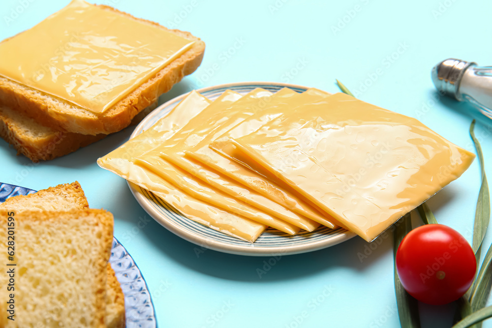 Plates of tasty processed cheese with bread and vegetables on blue background Plates of tasty processed cheese with bread and vegetables on blue background