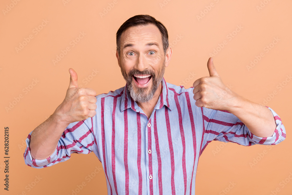 Photo of impressed man white gray hairstyle wear striped shirt showing thumbs up astonished staring isolated on beige color background Photo of impressed man white gray hairstyle wear striped shirt showing thumbs up astonished staring isolated on beige color background