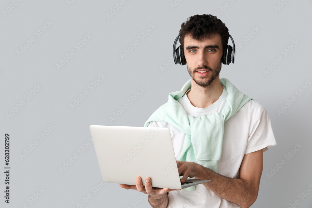 Young man in headphones working with laptop on light background Young man in headphones working with laptop on light background