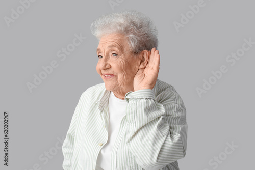 Fotografia Senior woman trying to hear something on grey background