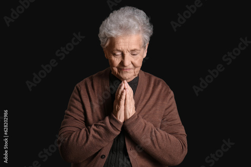 Senior woman praying on black background